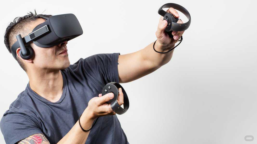 tattooed man with mohawk haircut in gray Tshirt wearing Oculus Touch VR headset holding controllers with thumb on buttons