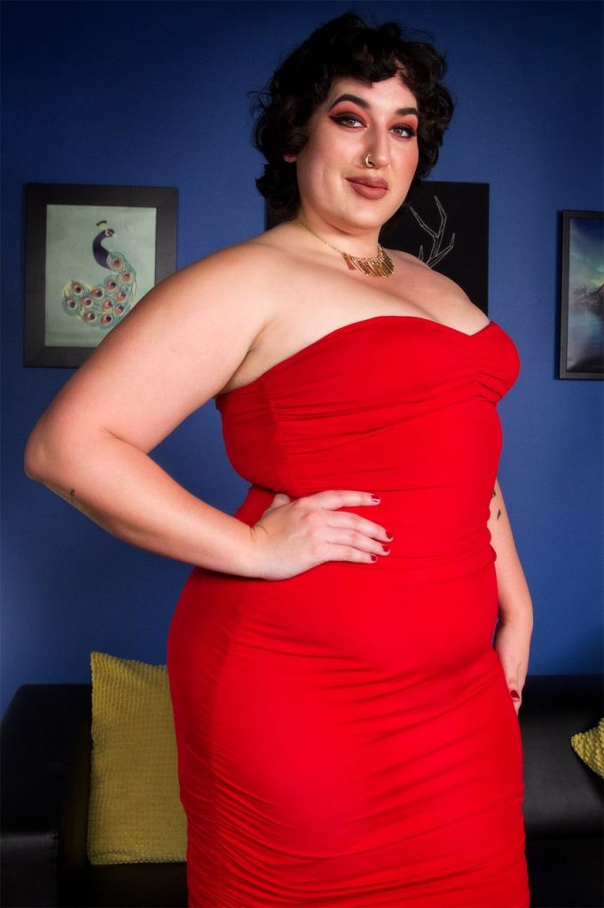 chubby Midnight Mimosa wearing a red dress and posing with her hand on her hip